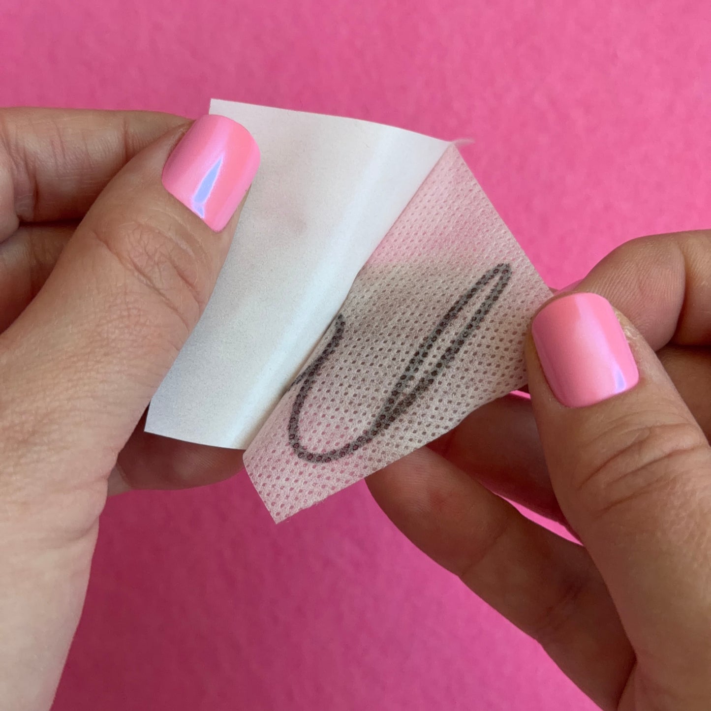 Hand holding a small piece of white paper with a black design against a pink background
