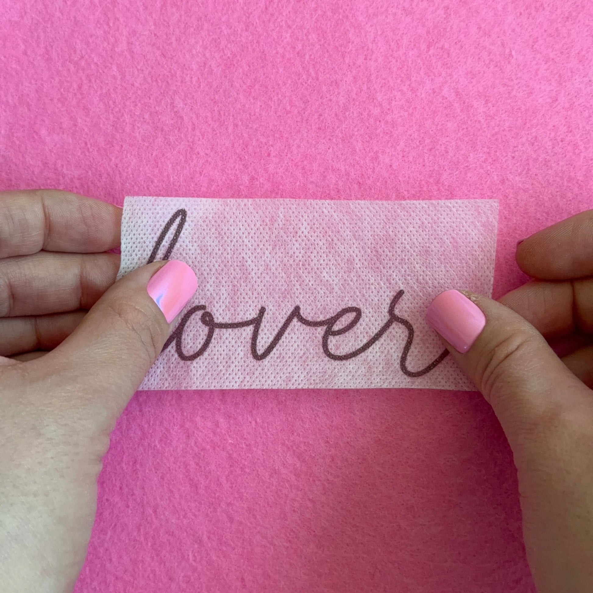 Hand holding a piece of paper with 'flowers' text against a pink background